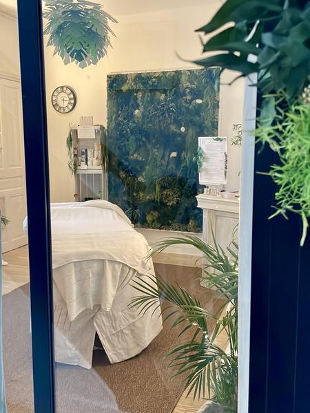 Un espace avec en son milieu une table de massage. Il y a des plantes, un mur de végétations.