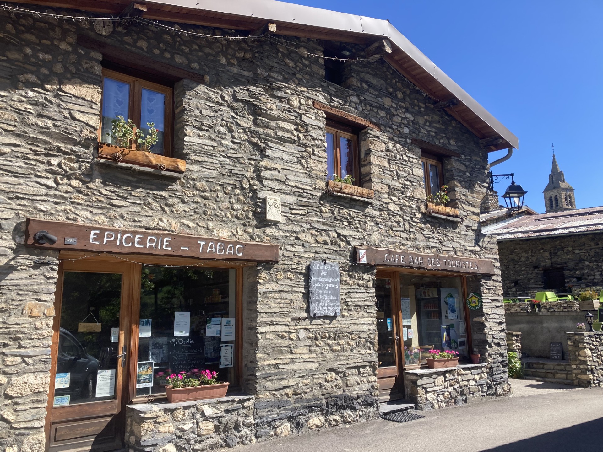 Maison en pierres dans le village de besse en oisans. Panneau en bois. Ciel bleu et clocher en arrière plan. Paysage d'été.