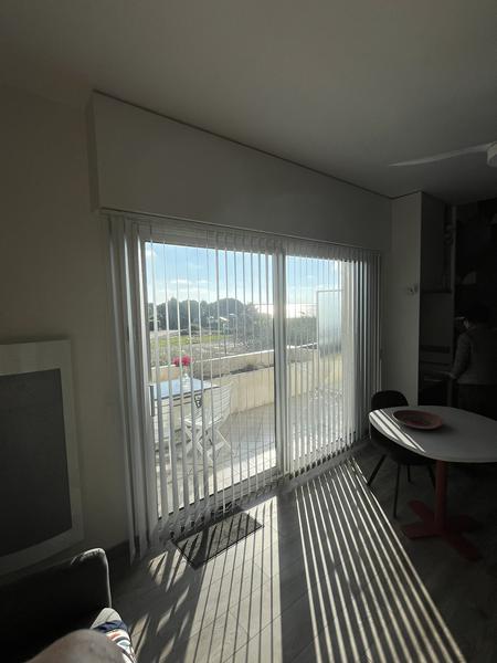 Vue sur l'extérieur depuis l'intérieur: vue sur le balcon, sa table et ses chaises en plastique,, et vue sur la mer
