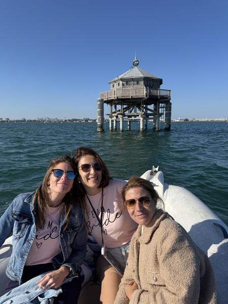 Trois femmes sur un bateau, en fond le phare du Bout du Monde.