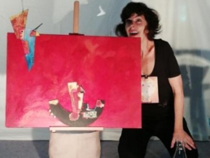 actrice habillée en noir manipulant un petit pinceau en papier derière un petit tableau rouge.