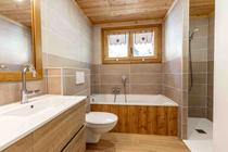 Salle de bains moderne et lumineuse avec baignoire, bac à douche, toilettes, ameublement bois, fenêtre